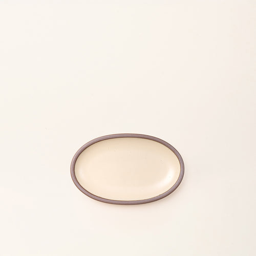 A small oval ceramic platter in a cream color featuring iron speckles and an unglazed rim