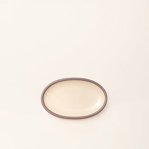 A small oval ceramic platter in a cream color featuring iron speckles and an unglazed rim