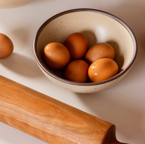 A dinner sized rounded ceramic bowl in a matte cream color featuring iron speckles and an unglazed rim.