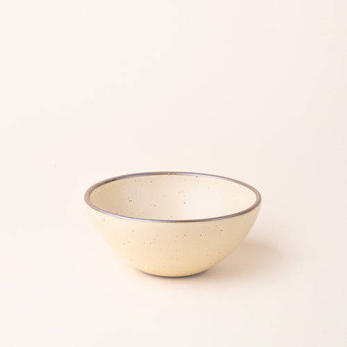 A dinner sized rounded ceramic bowl in a cream color featuring iron speckles and an unglazed rim