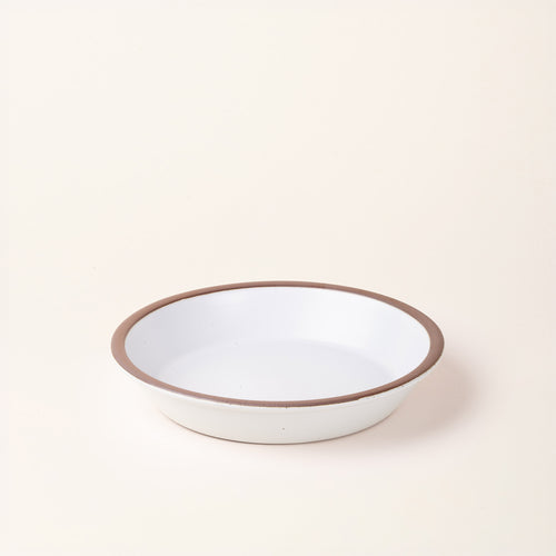 A shallow round ceramic pie plate in a matte cool white color featuring an unglazed rim, photographed against a cream background.