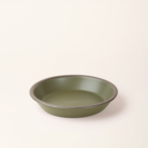 A shallow round ceramic pie plate in a olive green color featuring an unglazed rim, against a cream background.