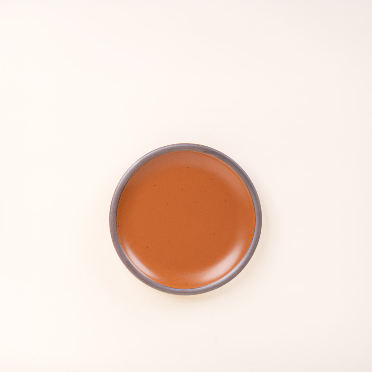 A dessert sized ceramic plate in an earthy orange color featuring iron speckles and an unglazed rim.