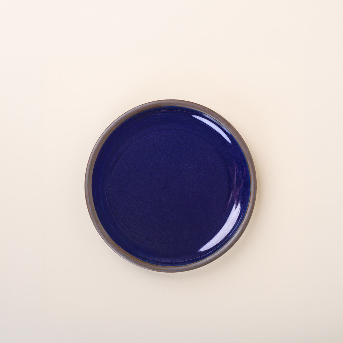 A medium sized ceramic plate in a glossy dark blue color featuring iron speckles and an unglazed rim.