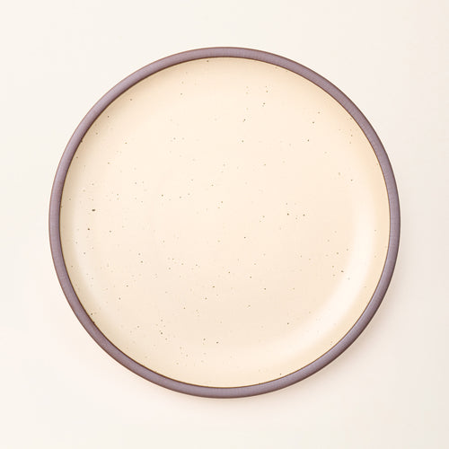 A large ceramic platter in a cream color featuring iron speckles and an unglazed rim.