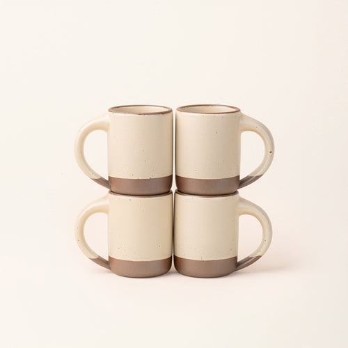 Four medium sized ceramic mugs with handles arranged together in a matte cream color featuring iron speckles, unglazed rims and bottom bases.