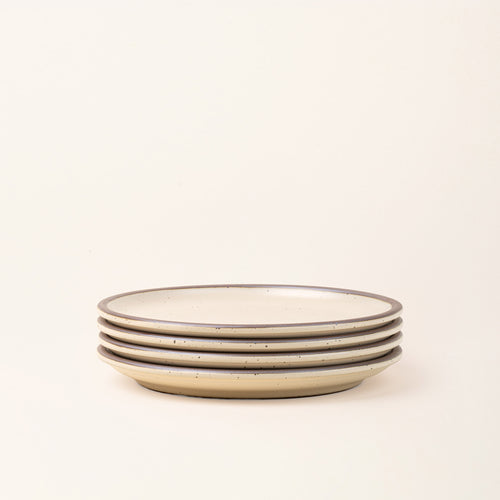 A stack of 4 dinner sized ceramic plates in a matte cream color featuring iron speckles and unglazed rims.
