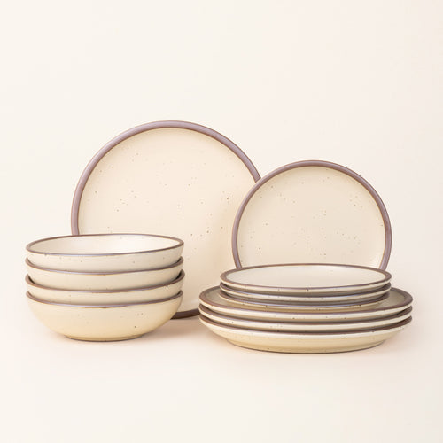 A set of stoneware dinnerware including four dinner plates, four side plates, and four bowls in a cream color with iron speckles.