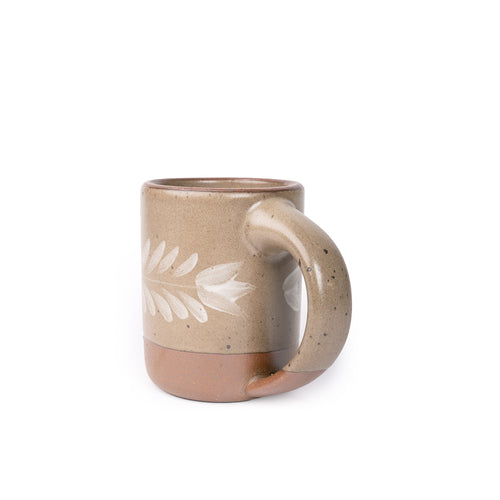 Side profile of a pale warm brown ceramic mug with a hand-painted white leaf motif and exposed clay base on a plain white background.