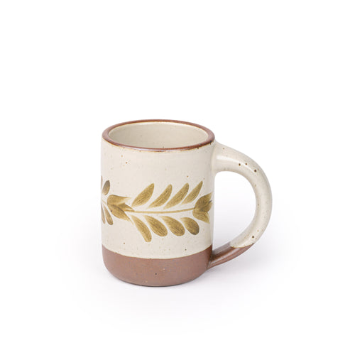 Warm off-white ceramic mug with a hand-painted olive green leaf motif and exposed clay base on a plain white background.