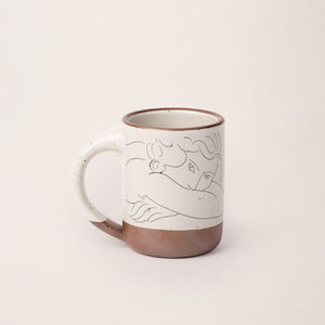 East Fork’s The Mug in a warm off white color with handle with a black decal of Henri Matisse’s Jeune femme la visage enfoui dans les bras, a bright blue, a line drawing of a young woman with face buried in her arms, on the body of the mug