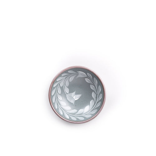 Overhead of a Small ceramic shallow bowl with a hand-painted white leaf border on a blue-grey interior and exterior with an exposed clay rim.