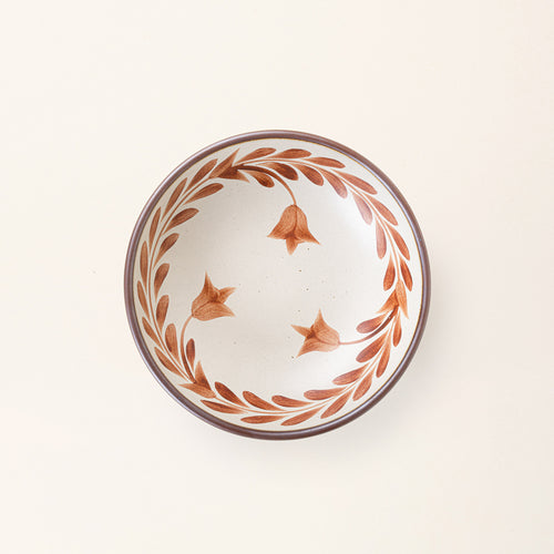 An overhead view of a Medium ceramic shallow bowl with a hand-painted terracotta leaf border on a cream interior and exterior with an exposed clay rim.