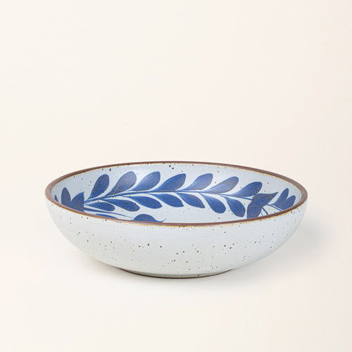 Large ceramic shallow bowl with a hand-painted blue leaf border on a white interior and exterior with an exposed clay rim.