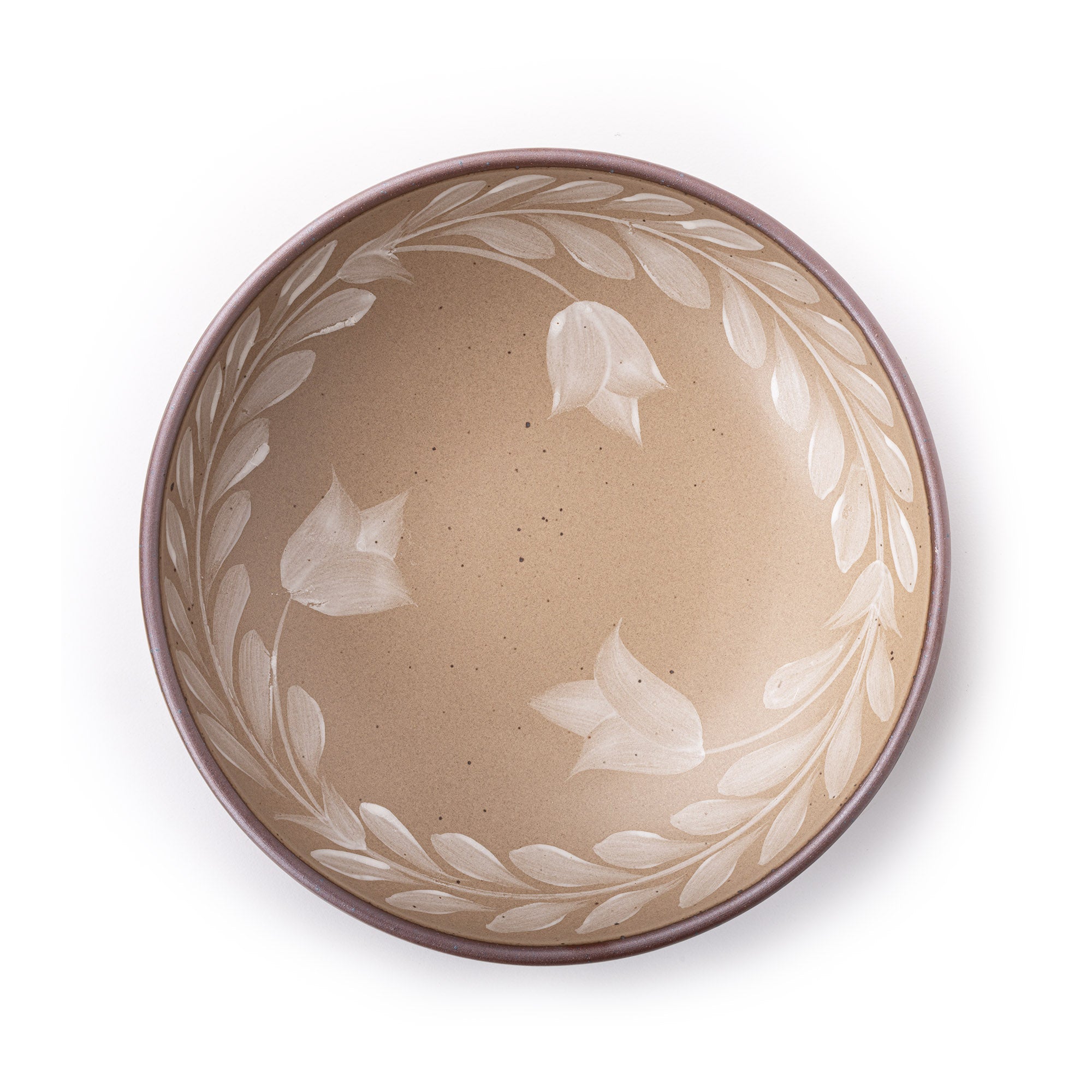 Overhead view of a large ceramic shallow bowl with a hand-painted white leaf border on a pale warm brown interior and exterior with an exposed clay rim.