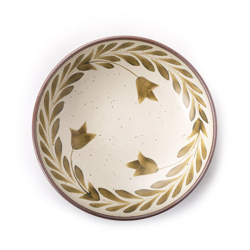 An overhead view of a large ceramic shallow bowl with a hand-painted olive green leaf border on a cream interior and exterior with an exposed clay rim.