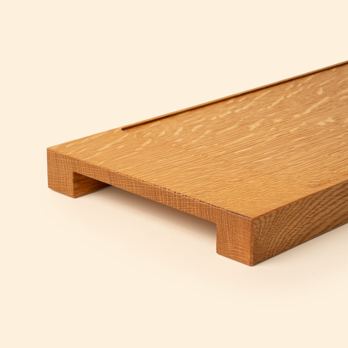 Close up of the handled edge of a narrow rectangle of light oak wood with a vertical groove at either end