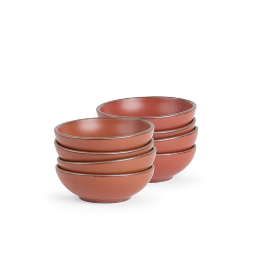 A stack of 8 small shallow ceramic bowls in a cool burnt terracotta color featuring iron speckles and an unglazed rim