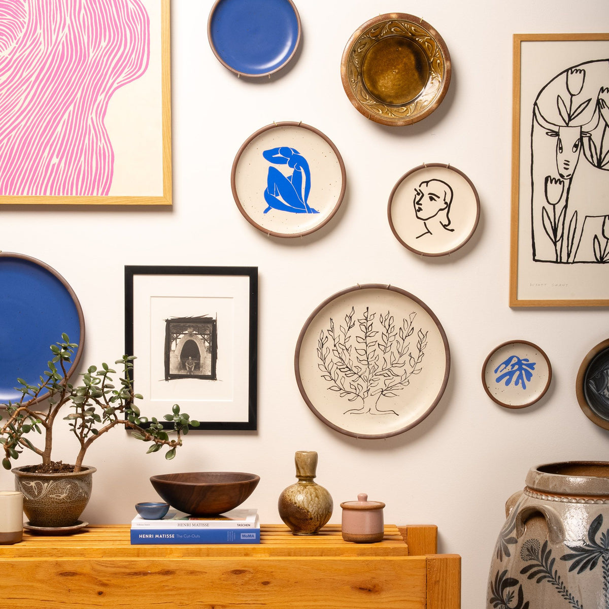 A gallery wall filled with artworks and hanging ceramic plates with works by Henri Matisse on them.