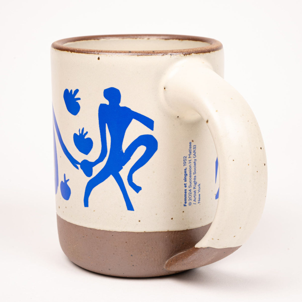 East Fork’s The Mug in a warm off white color with handle with a blue decal of Henri Matisse’s Femmes et singes and copyright, and a unglazed rim and bottom base.