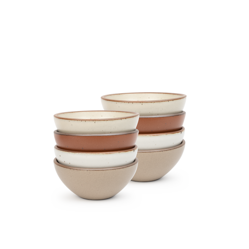 A stack of 8 small dessert sized rounded ceramic bowls in a cool terracotta, warm off-white, cool white, and warm pale brown colors featuring iron speckles and an unglazed rim