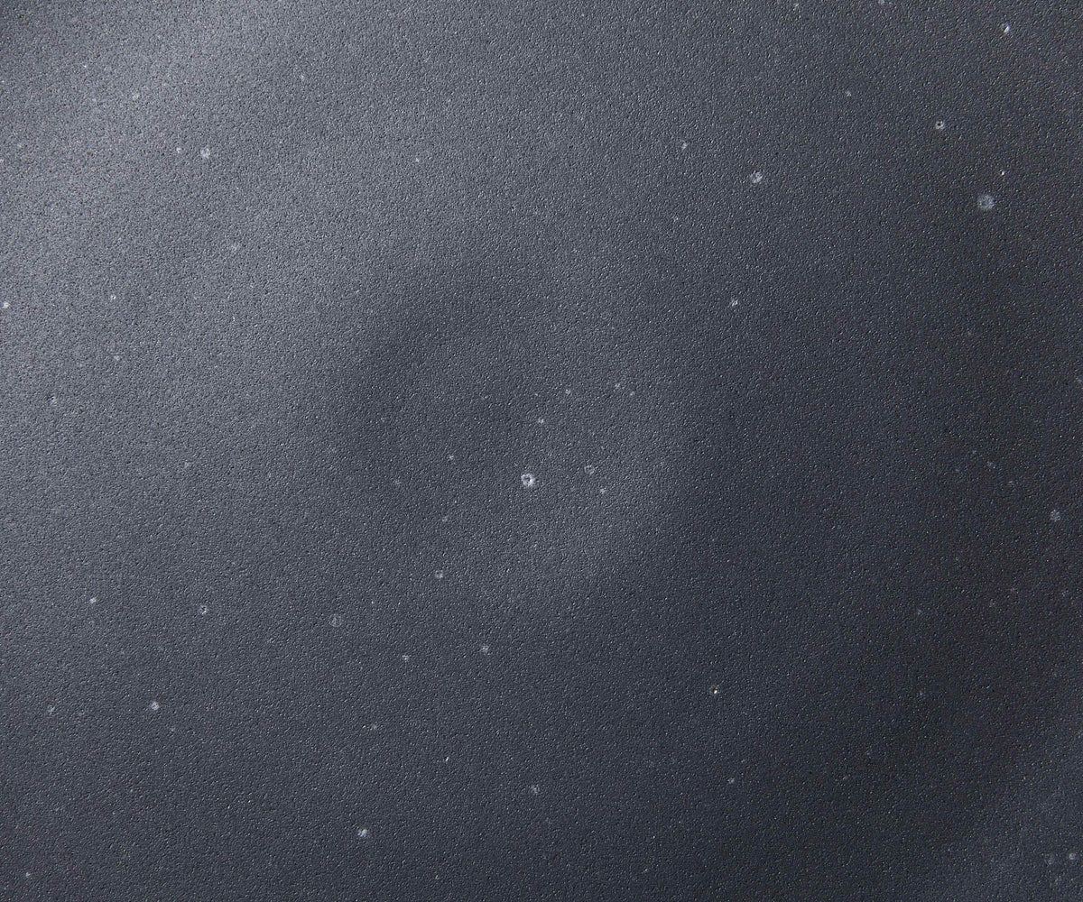 A closeup of a ceramic plate in a graphite black color with iron speckles throughout