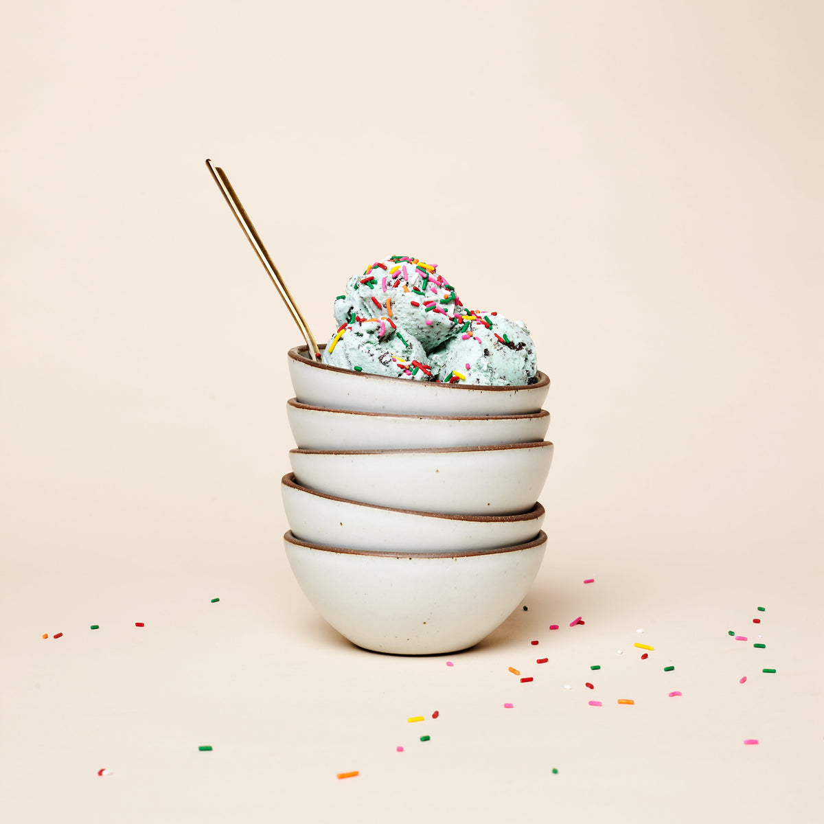 A stack of ceramic ice cream bowls with scoops of ice cream with sprinkles on top with a spoon.