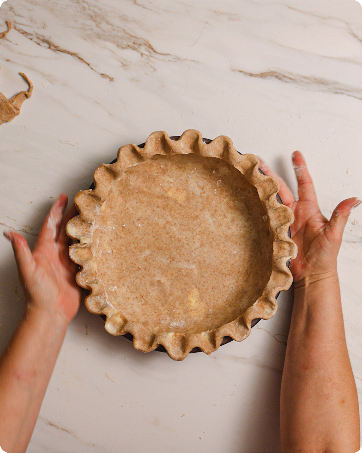 An overhead view of hands building a pie with pie crust that is crimped on the edges.