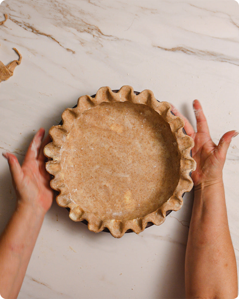 An overhead view of hands building a pie with pie crust that is crimped on the edges.