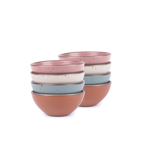 A stack of 8 small dessert sized rounded ceramic bowls in a cool terracotta, warm off-white, blue-grey and dusty mauve pink colors featuring iron speckles and an unglazed rim