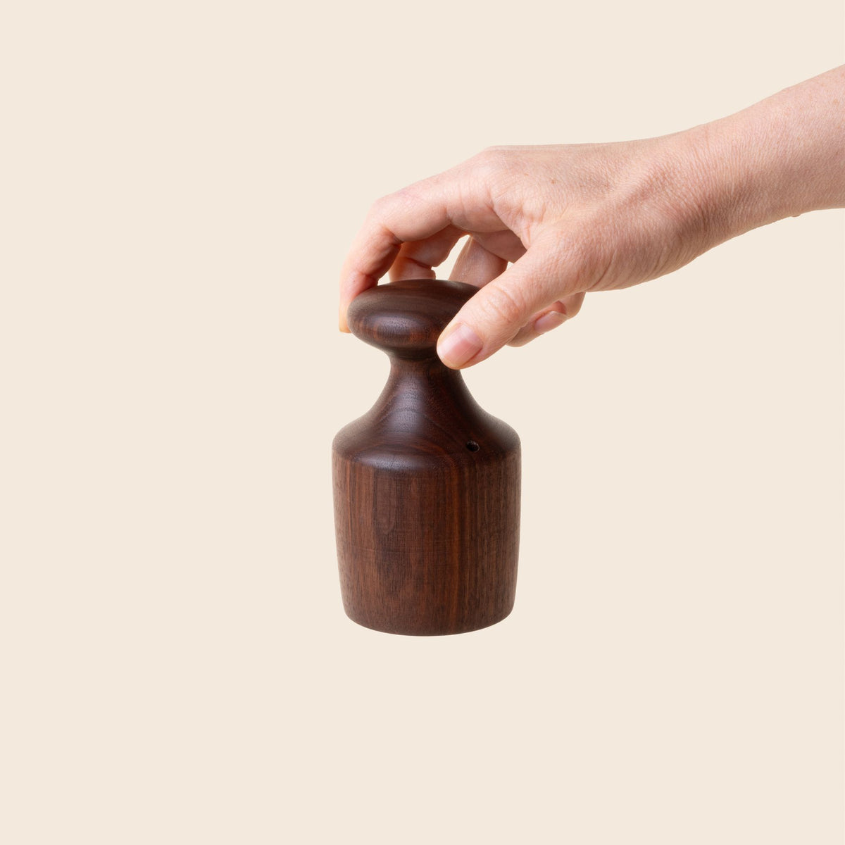 A hand holds a turned black walnut biscuit cutter with a knob at the top of a cylindrical black