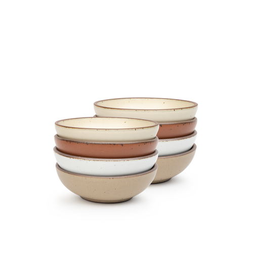 A stack of 8 small shallow ceramic bowls in a cool terracotta, warm off-white, cool white, and warm pale brown colors featuring iron speckles and an unglazed rim