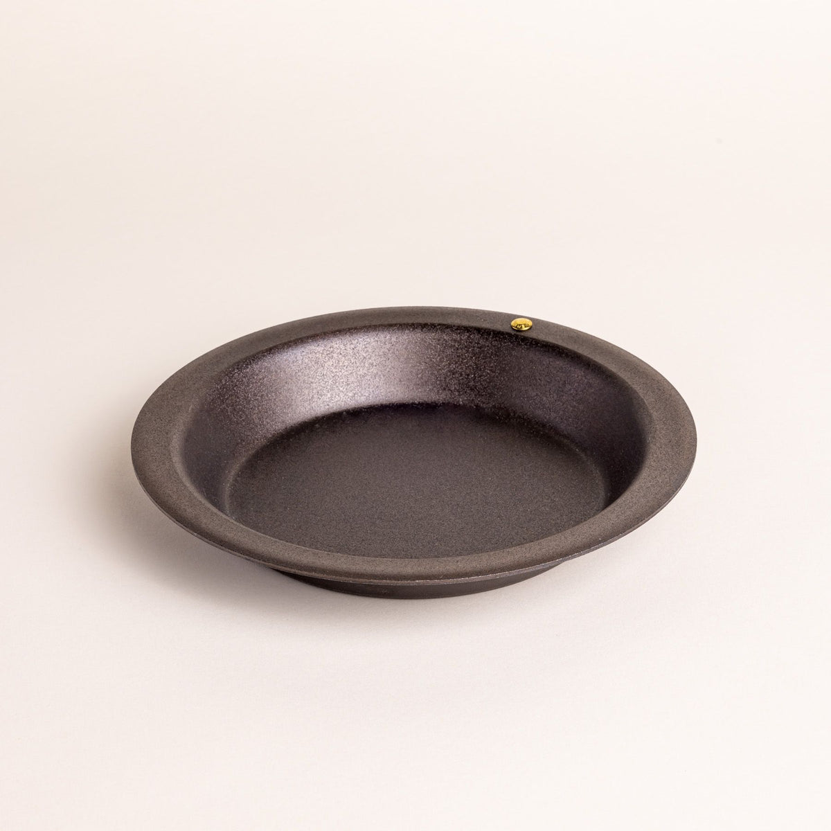 A small simple iron pie dish with a wide rim and shallow body