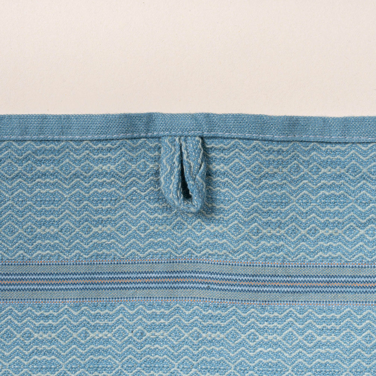 Close-up of a blue woven towel with a zigzag-and-diamond texture, stitched hanging loop, and thin striped band detail.