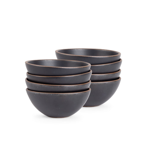 A stack of 8 medium rounded ceramic bowls in a graphite black color featuring iron speckles and an unglazed rim