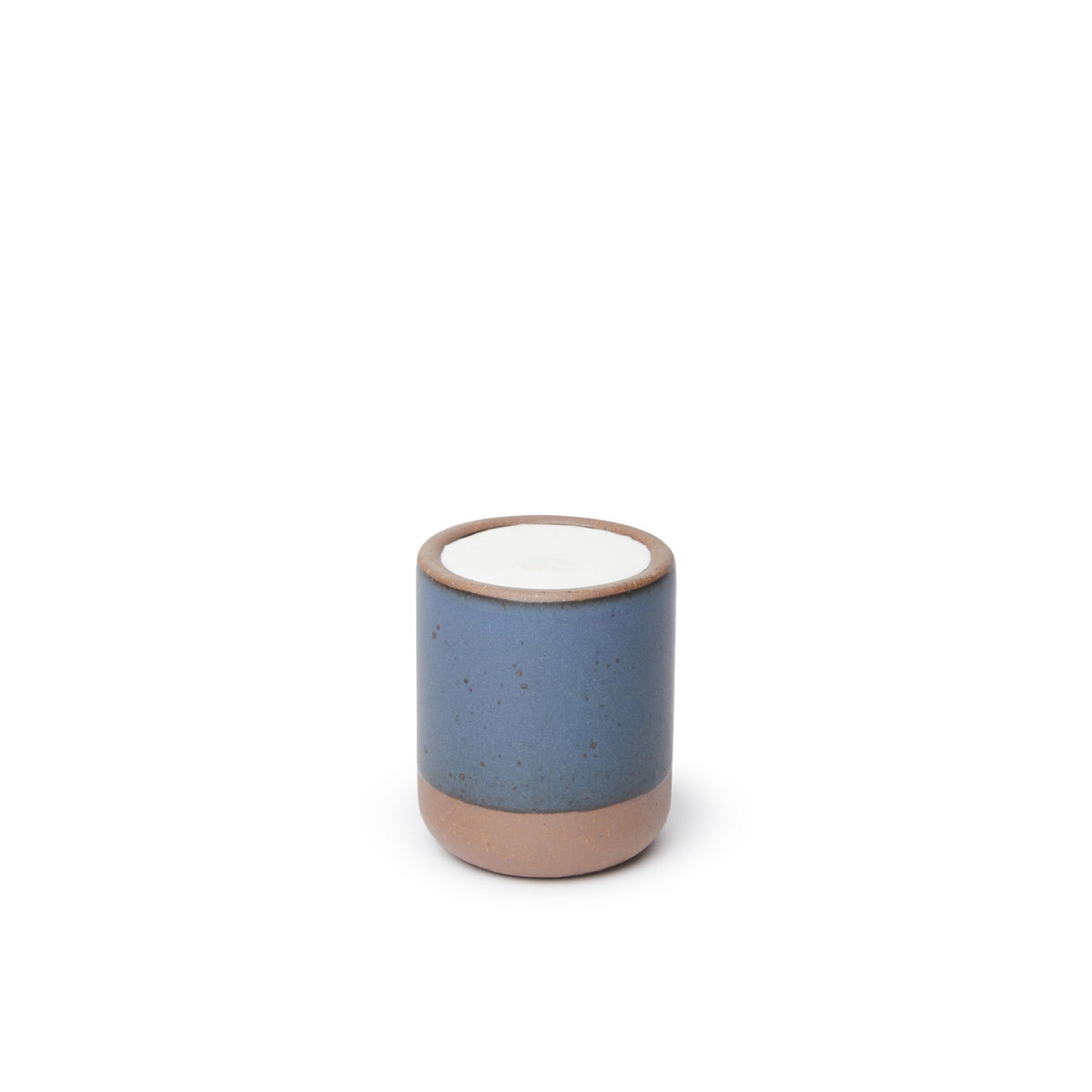 A small, short ceramic mug cup in a cool, medium blue color featuring iron speckles and unglazed rim and bottom base, filled with milk.