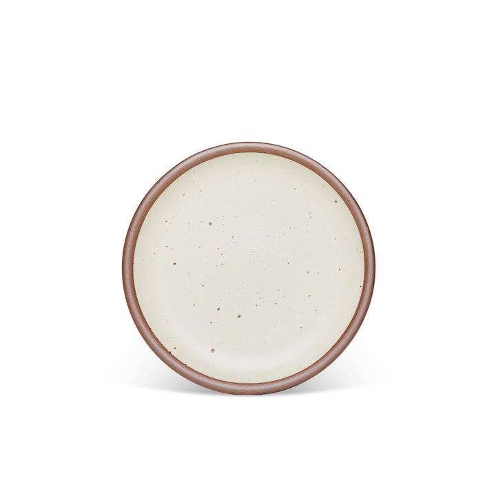 A medium sized ceramic plate in a warm, tan-toned, off-white color featuring iron speckles and an unglazed rim.