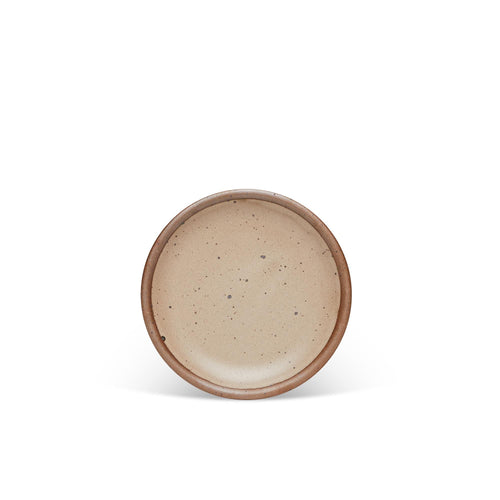 A dessert sized ceramic plate in a warm pale brown color featuring iron speckles and an unglazed rim.