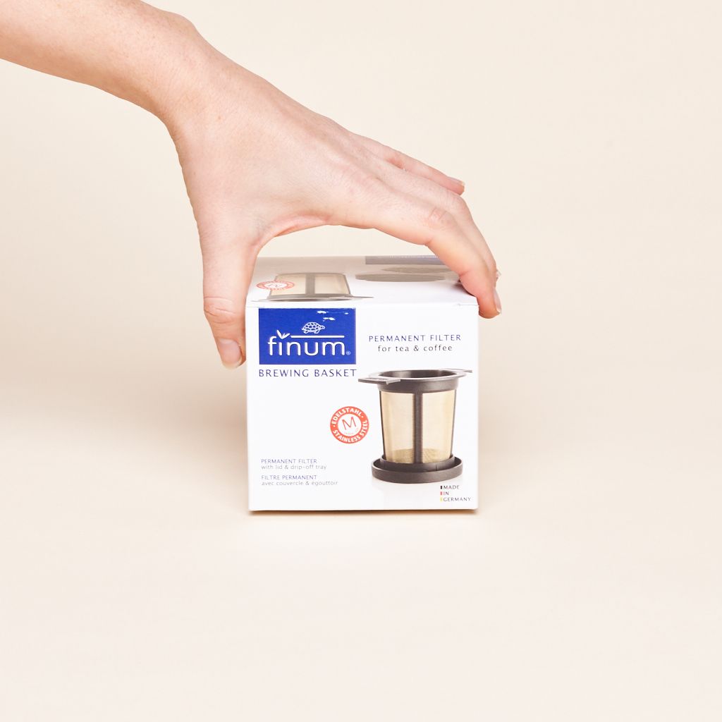 A hand holds the top of a box that says "Finum Brewing Basket" and has a photo of said basket